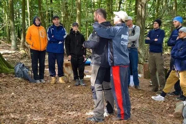 Zwei Personen demonstrieren eine Technik in einem Wald, umringt von Zuschauern
