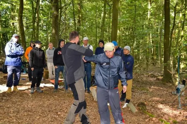 Zwei Personen demonstrieren eine Technik, während eine Gruppe im Hintergrund zuschaut