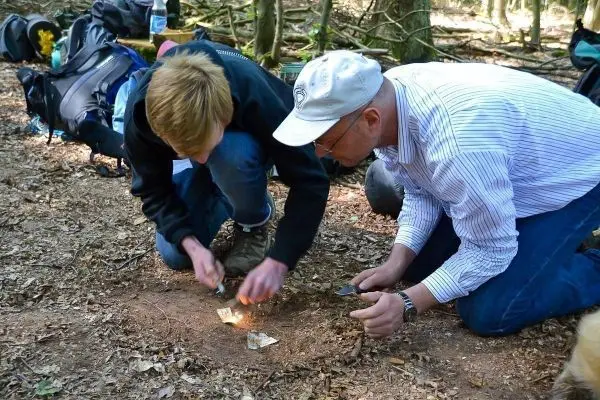 Zwei Personen entzünden ein Feuer auf dem Boden im Wald beim Survival Training