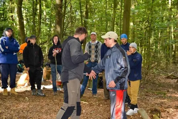 Zwei Personen führen eine Demonstration im Wald durch, während Zuschauer aufmerksam zuschauen