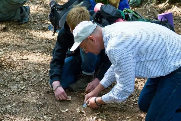 Zwei Personen knien am Boden und bearbeiten Zunder mit einem Messer
