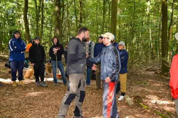 Zwei Personen schütteln sich die Hände im Wald, Zuschauer beobachten sie