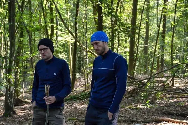 Zwei Personen stehen im Wald und halten Stöcke in der Hand