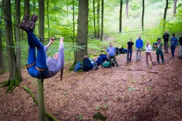Eine Person überquert eine selbstgebaute Seilbrücke zwischen zwei Bäumen