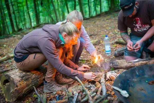 Feuerstahl erzeugt Funken auf Zunder im Wald, während zwei Personen konzentriert arbeiten