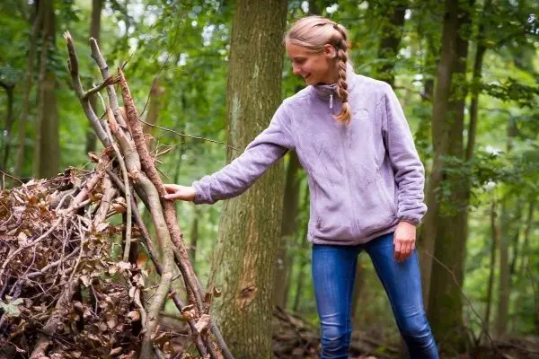Frau überprüft eine selbstgebaute Laubhütte im Wald