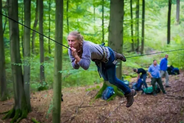 Frau überquert selbstgebaute Seilbrücke zwischen Bäumen im Wald