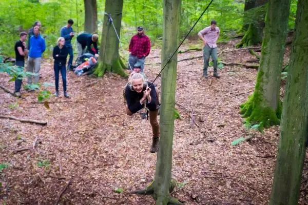 Frau überquert selbstgebaute Seilbrücke zwischen zwei Bäumen im Wald