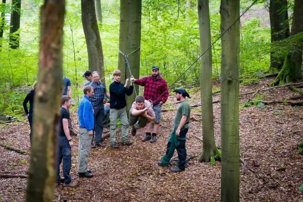 Gruppe von Personen um eine selbstgebaute Seilbrücke im Wald