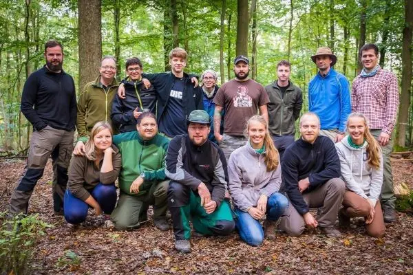 Gruppierung von Personen im Wald, umgeben von Bäumen und Laub