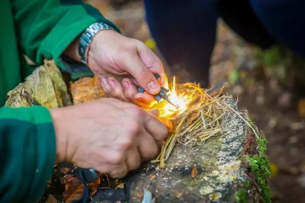 Hände entzünden trockenes Gras auf einem Baumstumpf beim Survival Training