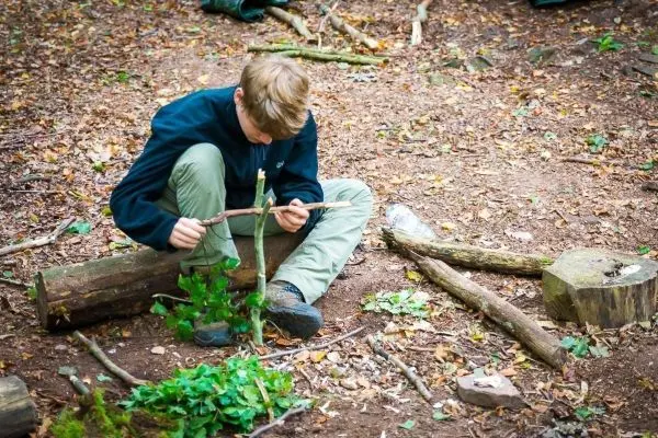 Junge bearbeitet einen Stock mit einem Messer auf dem Waldboden