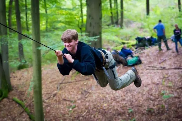 Junge überquert eine selbstgebaute Seilbrücke zwischen Bäumen
