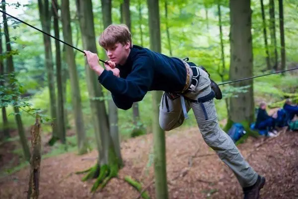 Junge überquert selbstgebaute Seilbrücke zwischen Bäumen im Wald