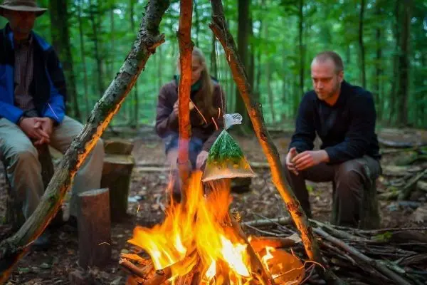 Kessel hängt über einem Feuer, während zwei Personen davor sitzen
