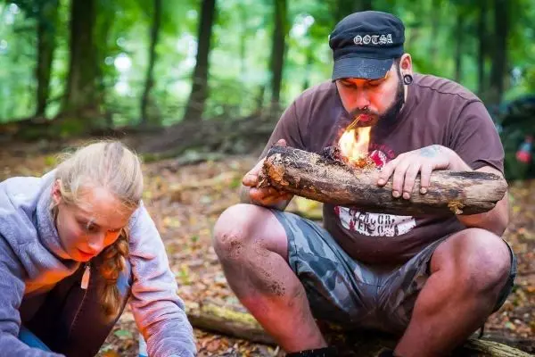 Kleines Bodenfeuer auf einem Holzstück, während eine Person Zunder vorbereitet