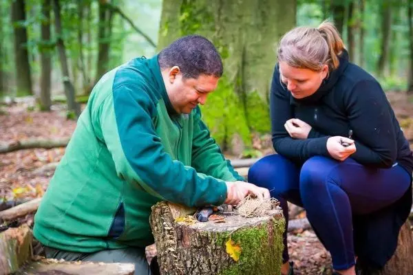 Mann bereitet Zunder auf einem Baumstumpf vor, Frau beobachtet aufmerksam