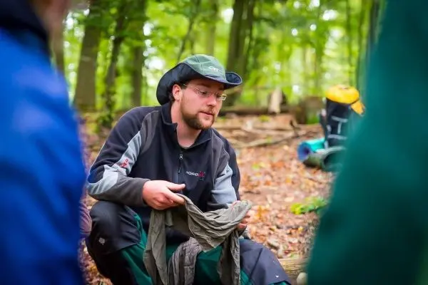 Mann hält ein Kleidungsstück in der Hand und erklärt etwas im Wald