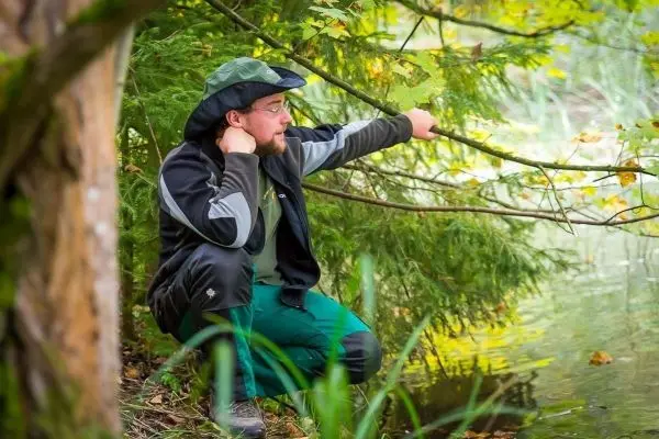 Mann hockt am Ufer und beobachtet das Wasser zwischen Bäumen