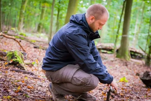 Mann kniet im Wald und hält ein Stück Holz in der Hand