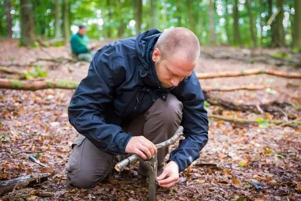 Mann konstruiert eine Schlagfalle aus Ästen im Wald