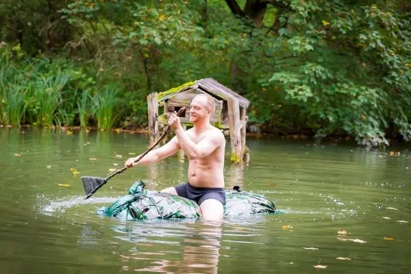 Mann paddelt auf improvisiertem Floß durch einen ruhigen Teich