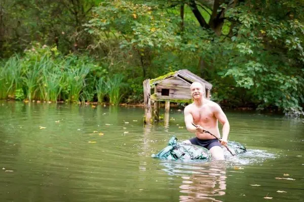 Mann paddelt auf improvisiertem Floß durch einen ruhigen Teich