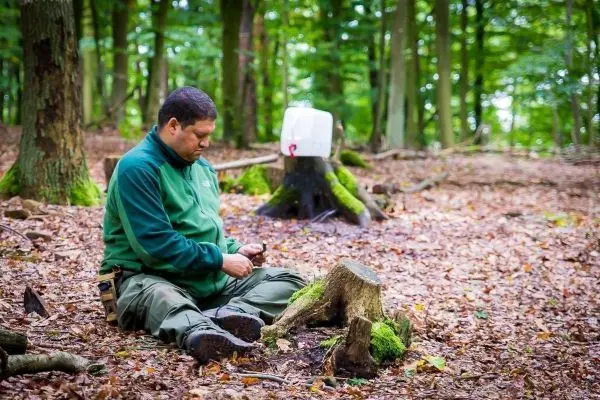 Mann sitzt auf dem Boden und schnitzt mit einem Messer an einem Holzstück