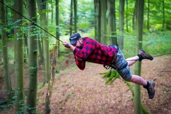 Mann überquert eine selbstgebaute Seilbrücke zwischen Bäumen