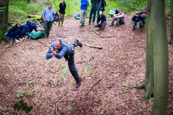 Mann überquert eine selbstgebaute Seilbrücke zwischen Bäumen