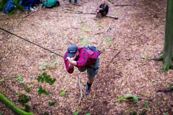 Mann überquert eine selbstgebaute Seilbrücke zwischen Bäumen
