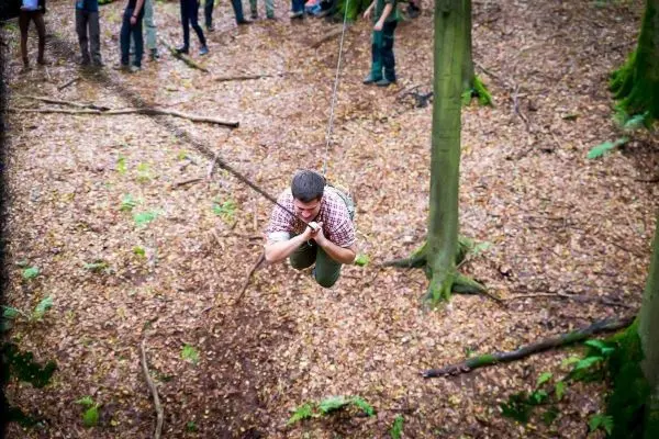 Mann überquert mit Seil eine Lichtung im Wald