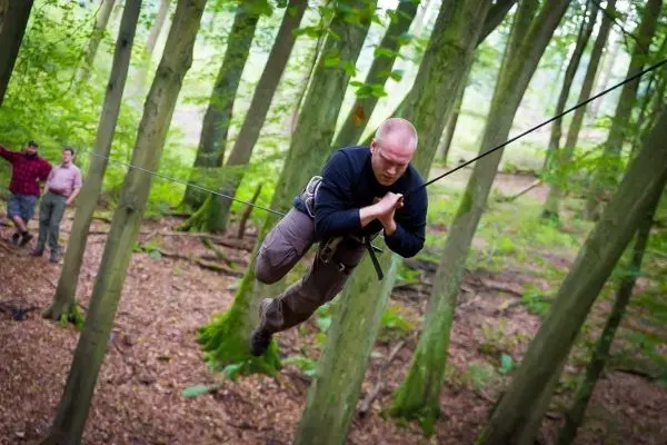 Mann überquert selbstgebaute Seilbrücke zwischen Bäumen im Wald
