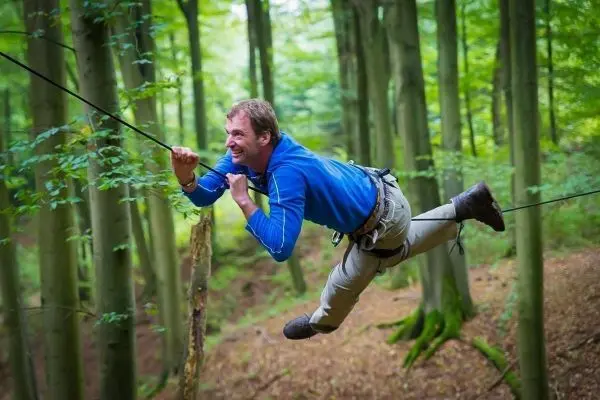 Mann überquert selbstgebaute Seilbrücke zwischen Bäumen im Wald