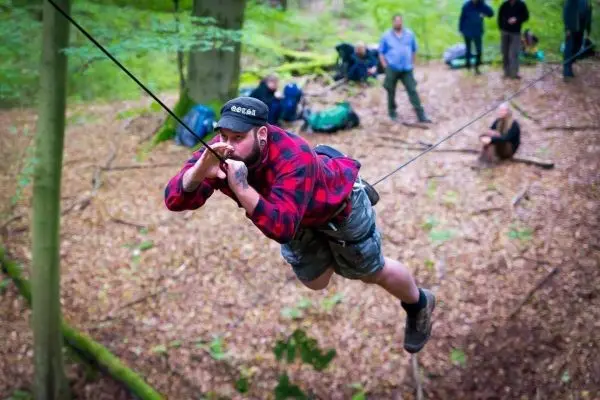 Mann überquert selbstgebaute Seilbrücke zwischen Bäumen im Wald