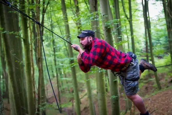 Mann überquert selbstgebaute Seilbrücke zwischen Bäumen im Wald