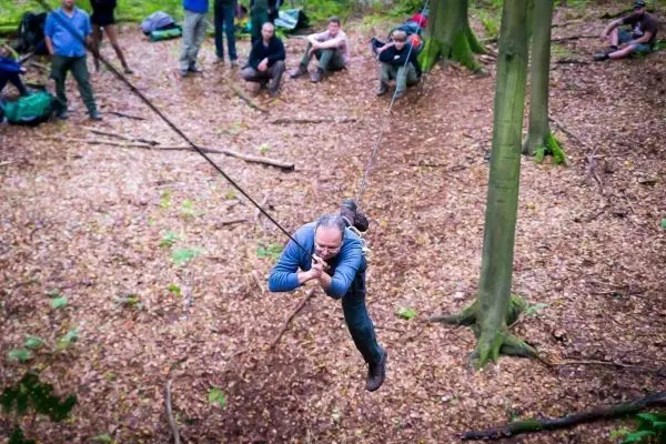 Mann überquert selbstgebaute Seilbrücke zwischen Bäumen im Wald