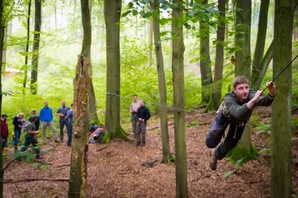 Mann überquert selbstgebaute Seilbrücke zwischen Bäumen im Wald