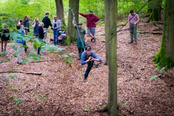 Mann überquert selbstgebaute Seilbrücke zwischen Bäumen im Wald
