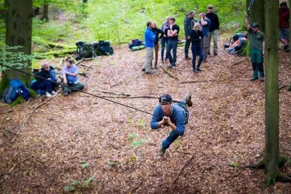 Mann überquert selbstgebaute Seilbrücke zwischen Bäumen im Wald