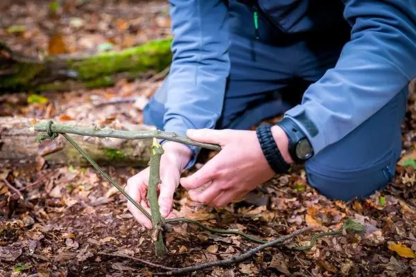 Person baut eine selbstgebaute Falle aus Ästen im Wald