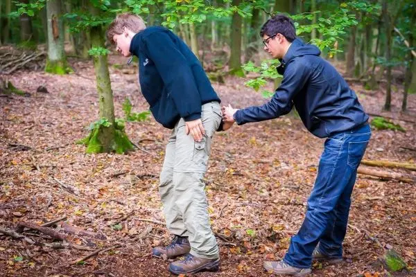Person hilft anderer Person beim Aufstehen im Wald