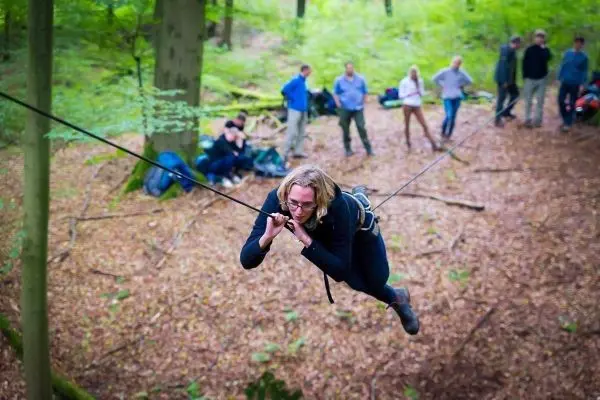 Person überquert selbstgebaute Seilbrücke zwischen Bäumen im Wald