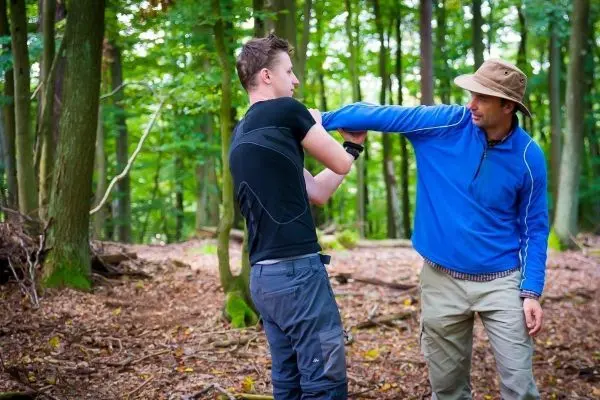Person zeigt einer anderen Person eine Technik im Wald