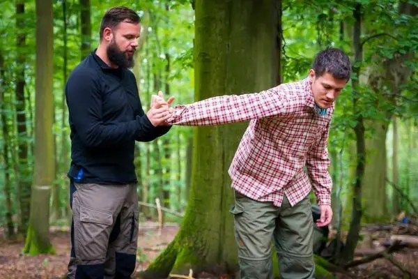 Person zeigt einer anderen Person eine Technik im Wald