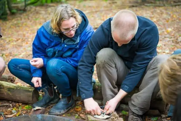 Person zeigt einer anderen Person, wie man Feuer macht beim Survival Training