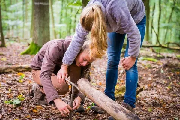 Person zündet mit einem Stock Feuer im Wald beim Survival Training