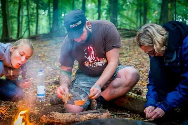 Personen bereiten Essen am Feuer im Wald vor beim Survival Training