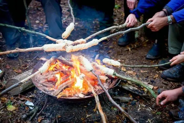 Personen halten Stöcke mit Teig über ein Feuer beim Kochen im Freien