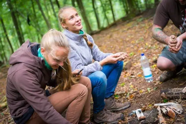 Personen sitzen im Wald und bearbeiten Holzstücke beim Überlebenstraining